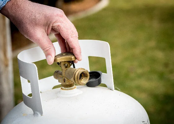 Hand turns a valve on a propane tank